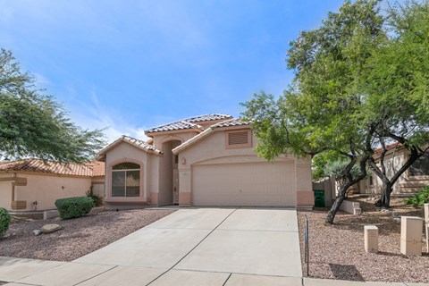 a beige house with a driveway and trees