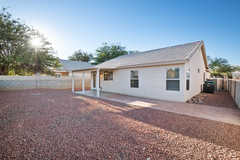 A house with a white exterior and a grey roof is surrounded by a gravel driveway.