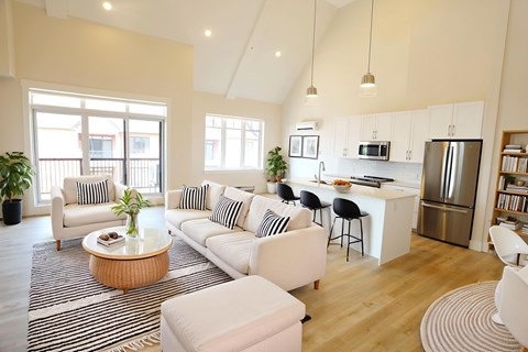 A modern living room with a kitchen in the background.
