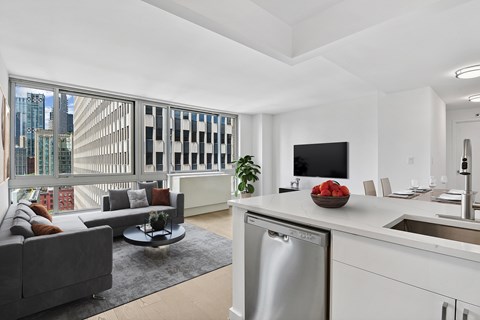 A modern kitchen with a dining table and chairs, a couch, and a large window with a view of the city.