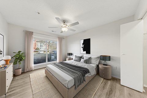 A bedroom with a large bed, a ceiling fan, and a window with a view of a backyard.