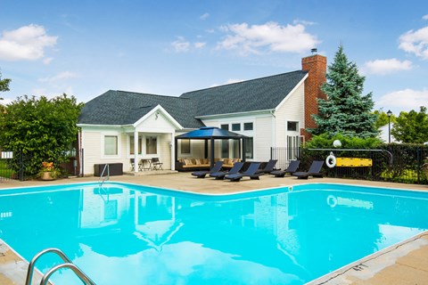 a swimming pool with chairs in front of a house