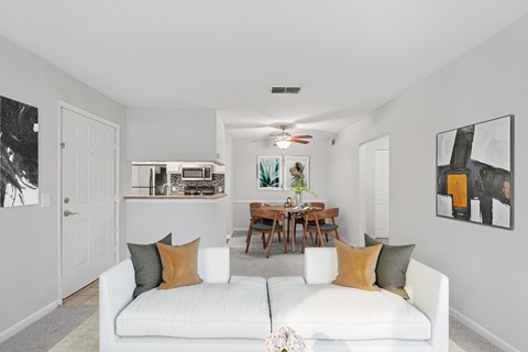 A living room with a white couch and a dining table in the background.