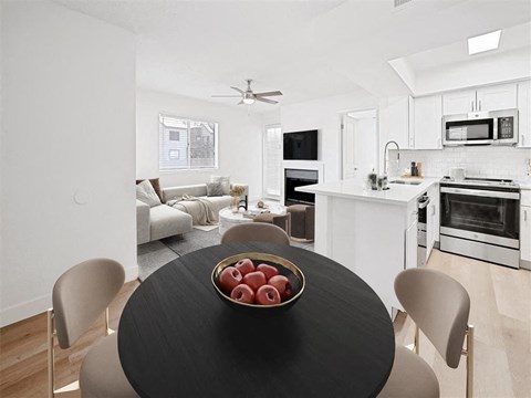 A modern kitchen with a black table and chairs, a bowl of apples, and a fan on the ceiling.
