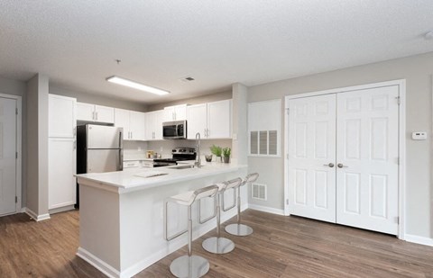 A kitchen with white cabinets and a white island with a bar stool.