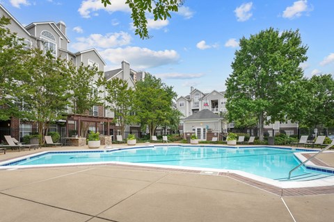 A large swimming pool surrounded by lounge chairs and trees in front of a building.