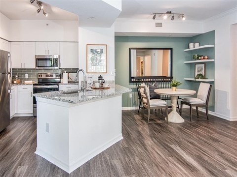 A kitchen with a white island and a dining table with chairs.