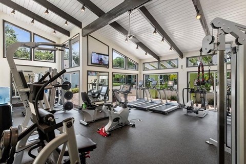 A spacious and light filled fitness center with a variety of equipment and a television mounted on the wall.