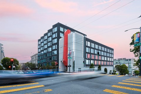 A modern building with a red and black design on the side stands on a street corner.