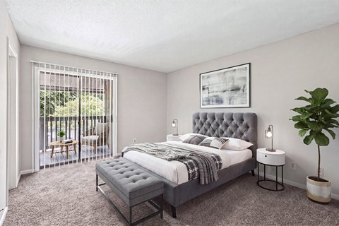 A bedroom with a bed, nightstand, and a plant.