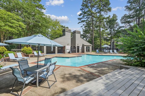 A pool surrounded by trees and chairs.