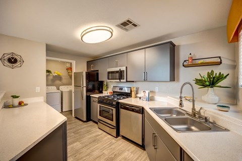 A kitchen with a stove top oven, microwave and a refrigerator.  The laundry room is in the background.