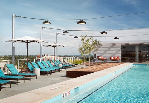 A pool with blue chairs and umbrellas is surrounded by a white building.