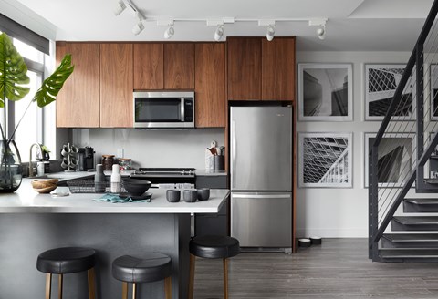 A modern kitchen with a stainless steel refrigerator and black bar stools.