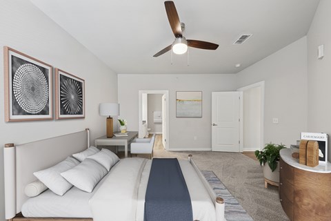 A bedroom with a bed, a ceiling fan, and a nightstand with a lamp.