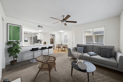 A living room with a grey couch, a round table, and a ceiling fan.