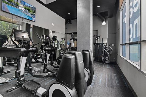 A gym with treadmills, elliptical machines, and a television.