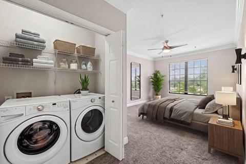 A laundry room with a washer and dryer and a bedroom with a bed and a ceiling fan.