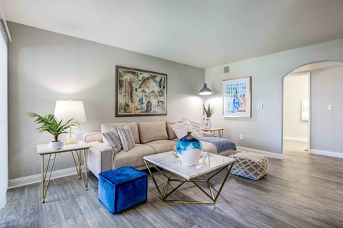 A living room with a white couch, a blue ottoman, and a painting on the wall.