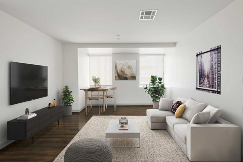 A modern living room with a grey sofa, a coffee table, a wooden dining table, and a flat-screen TV.