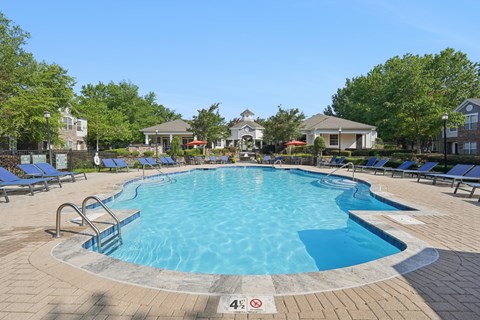 A swimming pool surrounded by a brick patio and lounge chairs.