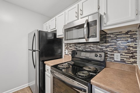 A black refrigerator and microwave are mounted above a stove in a kitchen.