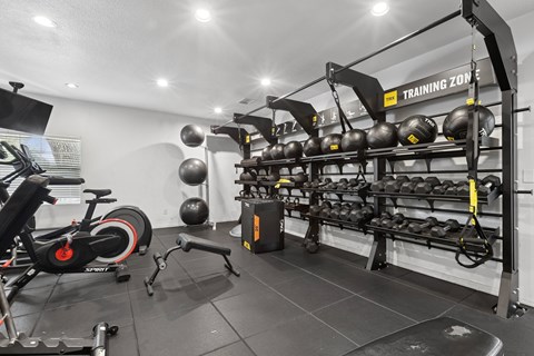 A gym with a row of kettlebells and a stationary bike.