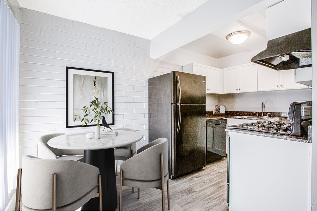 A kitchen with a black refrigerator, white cabinets, and a round table with chairs.