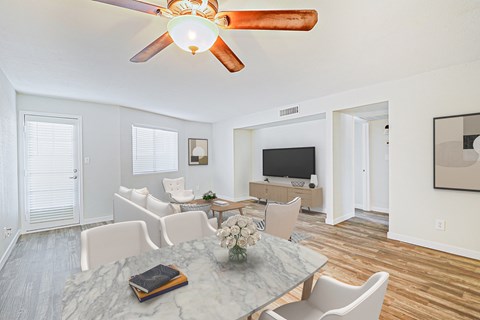 A living room with a ceiling fan and a dining table with chairs.