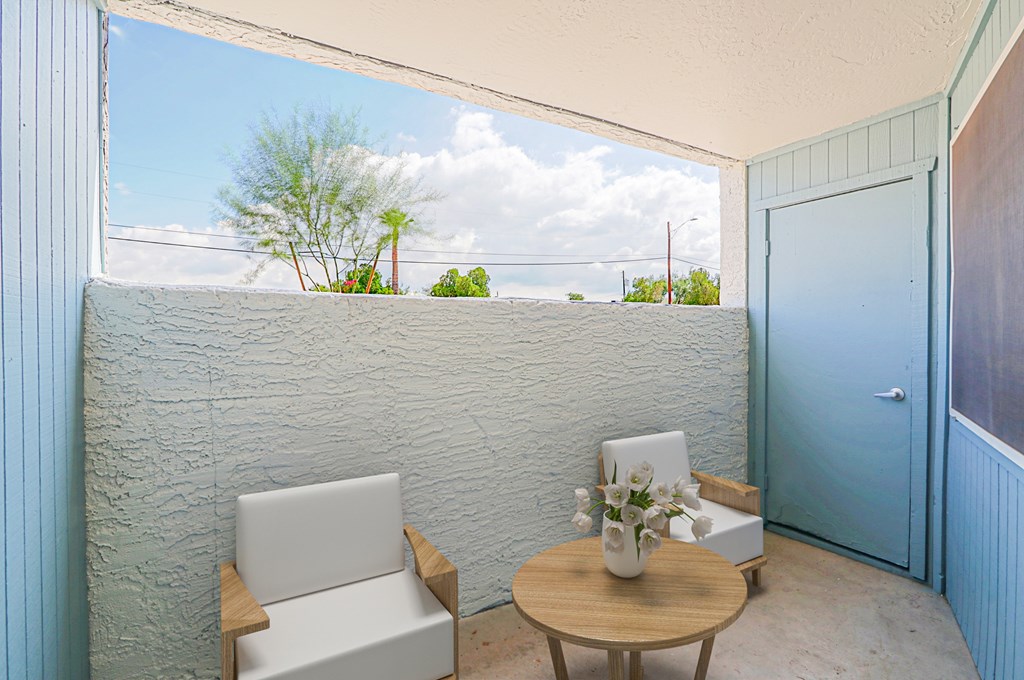 A patio with a white chair and a small table with a vase of flowers on it.