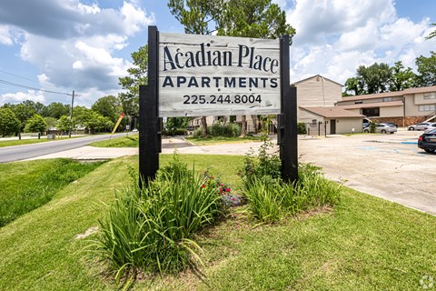 A sign for Acadian Place Apartments stands in front of a building.
