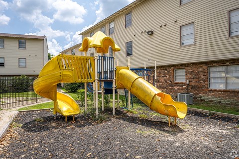 A yellow slide in a playground with a building in the background.