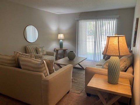 A living room with a tan couch, a wooden table, and a lamp.