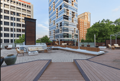 A wooden deck with chairs and a table in the middle of a courtyard surrounded by buildings.