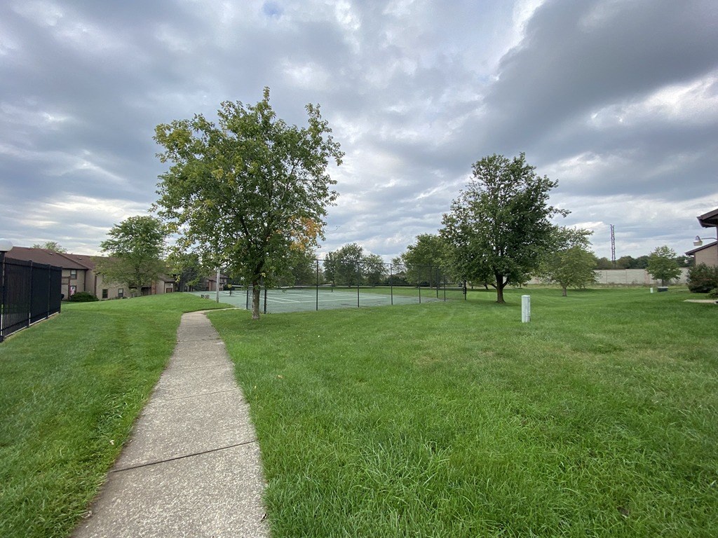 a sidewalk leading into a park with trees and a fence