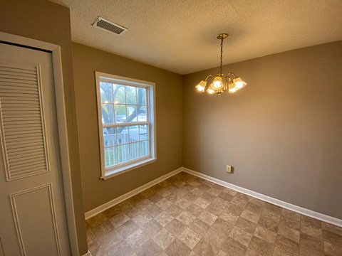 an empty dining room with a window and a chandelier