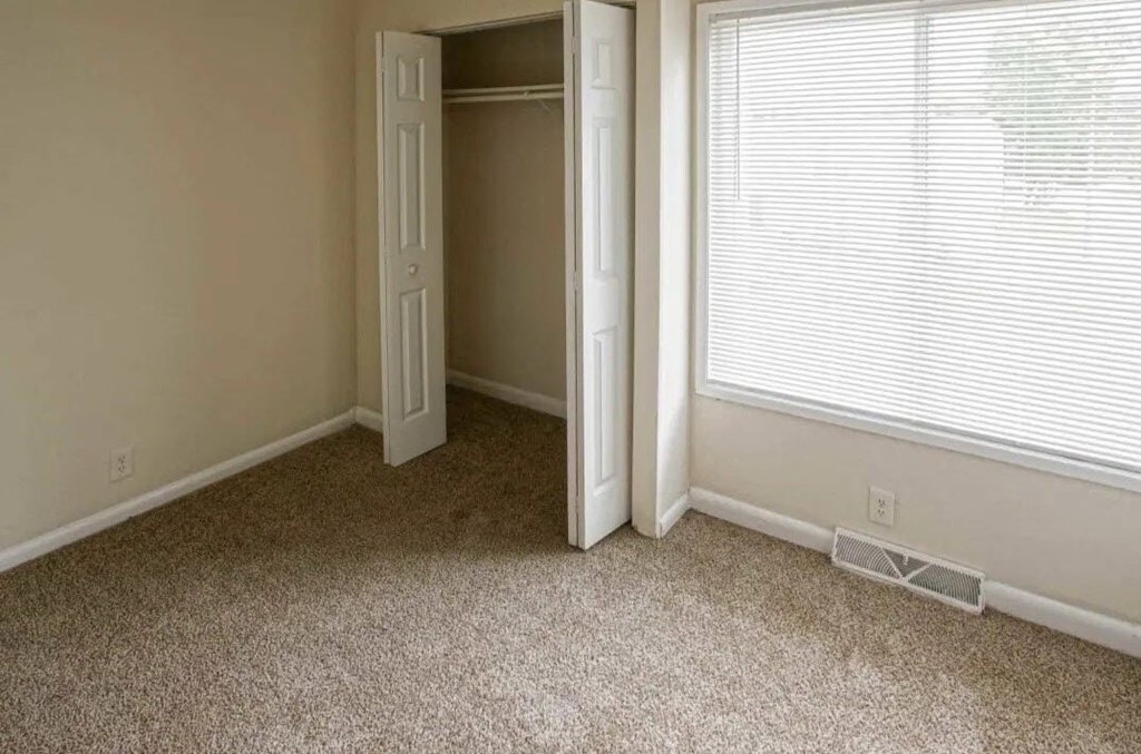 a bedroom with a closet and a window and a carpeted floor