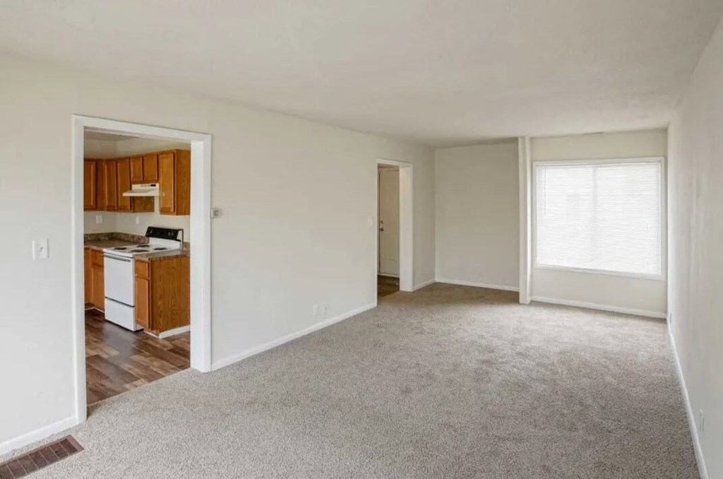 an empty living room with a kitchen in the background