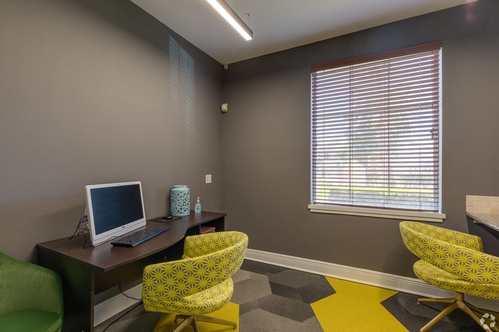 A room with a desk, chairs and a computer.