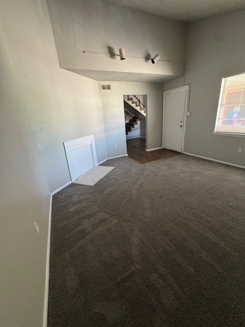 A room with a carpeted floor and a staircase in the background.