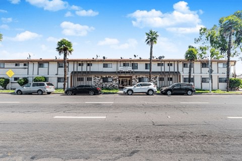 A parking lot with cars and a building with palm trees in front.