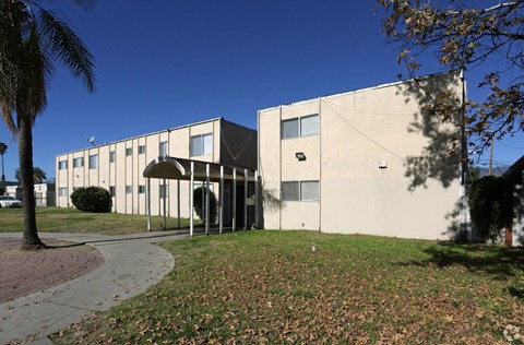 A building with a white and beige exterior is surrounded by a grassy area with fallen leaves.