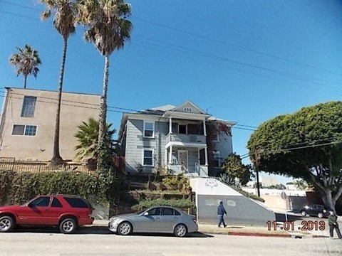 A red car is parked on the left side of a street, and a silver car is parked on the right side.