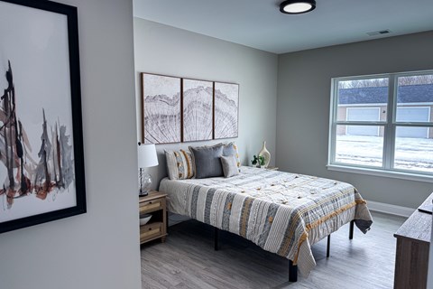 A bedroom with a bed, nightstand, and a painting on the wall.