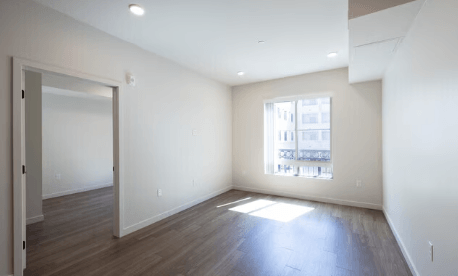 A large empty room with a window and wooden floors.