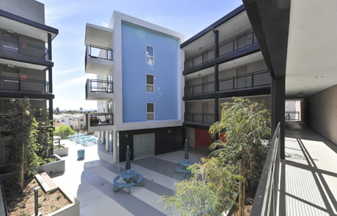 A modern building with a blue and white exterior is surrounded by other buildings and greenery.
