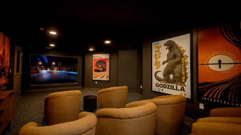 A room with a screen, chairs and posters of Godzilla.