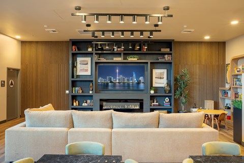 A room with a large couch, a coffee table, and a bookshelf with a cityscape picture on it.