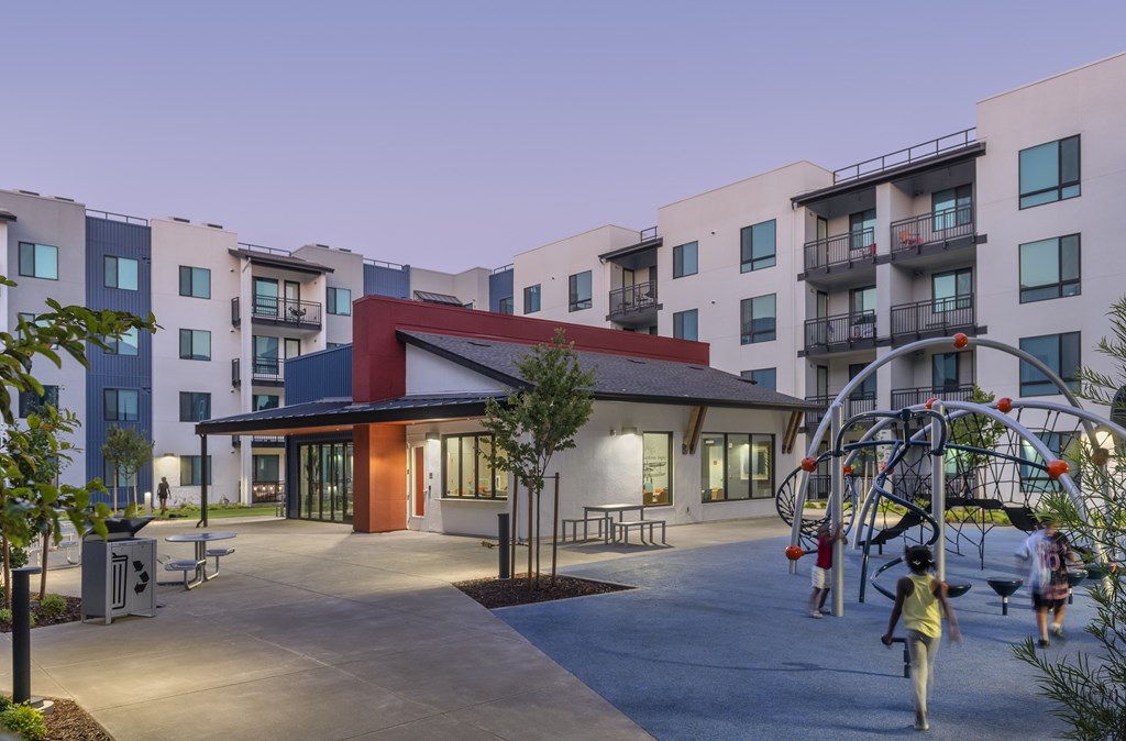 A playground with a swing set and a building with a red awning in the background.