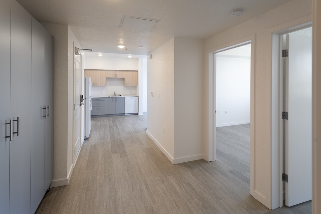 A long hallway with white doors and a kitchen in the background.